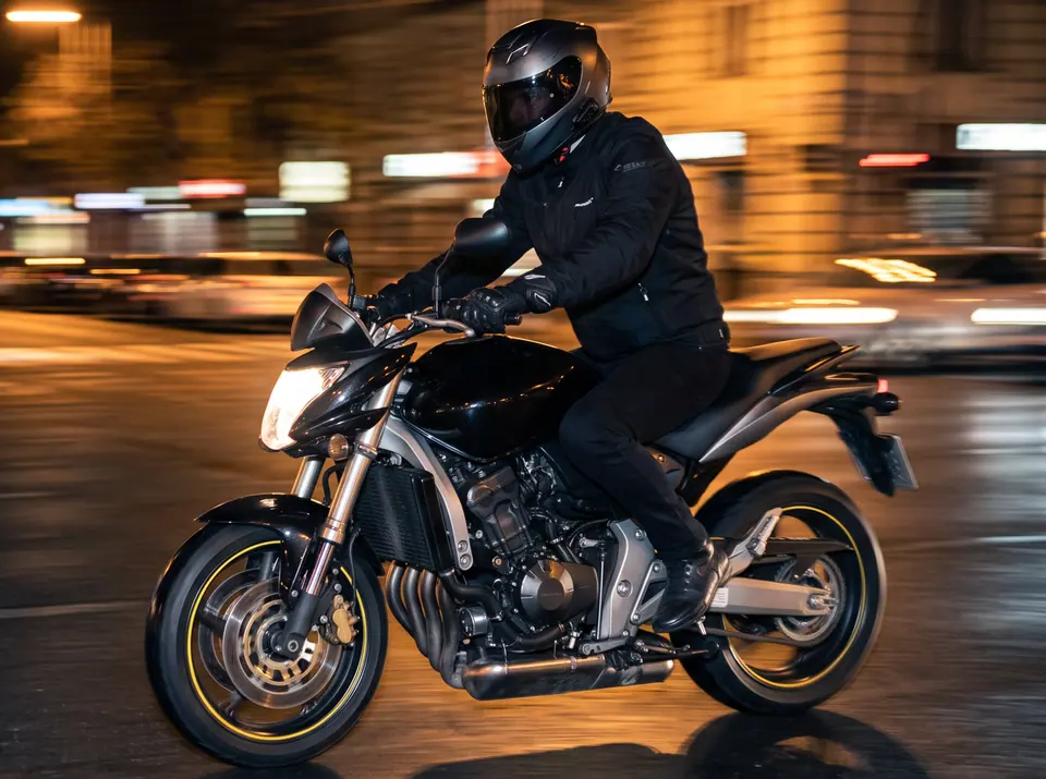Piloto numa moto naked de 4 cilindros estilo Hornet passando à noite por uma rua da cidade (imagem ilustrativa)